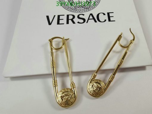 Gold safety-pin style earrings on branded backdrop.