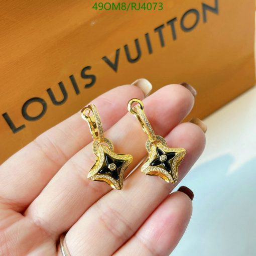 Gold star-shaped earrings held near branded box.