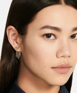 Woman wearing designer earrings and blue shirt.