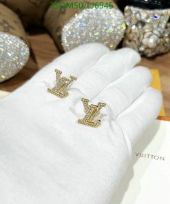 Gold initial earrings on gloved hand against sequined backdrop.