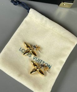 Gold flower-shaped earrings on branded pouch.