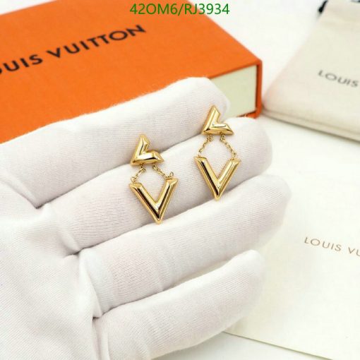 Gold designer logo earrings on white gloves.