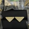 Gold triangular designer earrings with crystals on black background.