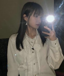 Woman taking mirror selfie with flash, wearing white shirt.