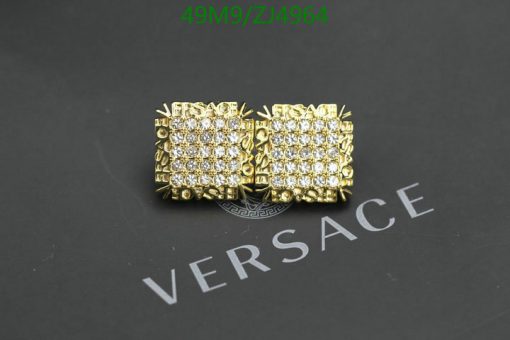 Gold Versace cufflinks with crystals on dark background.