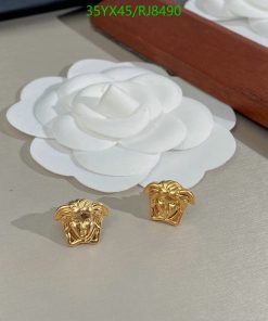 Gold lion head earrings on white surface.