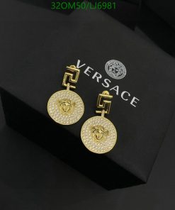 Gold designer earrings on black box with logo.