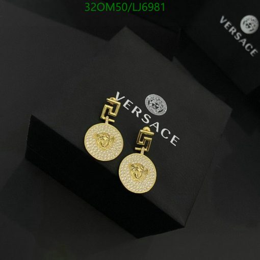 Versace gold medallion earrings on black background.