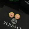 Gold and pink Versace medusa earrings on black background.