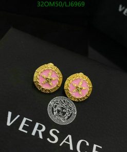 Gold and pink Versace medusa earrings on black background.