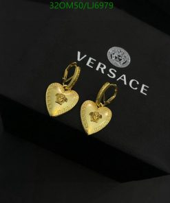 Gold heart-shaped Versace earrings on black background.