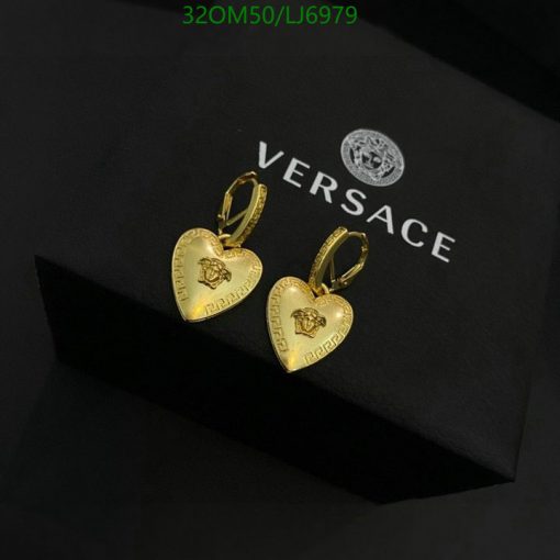 Gold heart-shaped Versace earrings on black background.