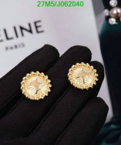 Gold earrings displayed on black gloves with Celine Paris logo.