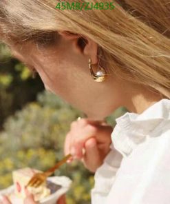 Woman eating, gold earring, outdoor setting.