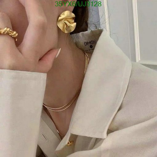 Woman wearing gold earrings and necklace with cream shirt.