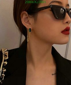 Woman with sunglasses, red lipstick, and green earrings.