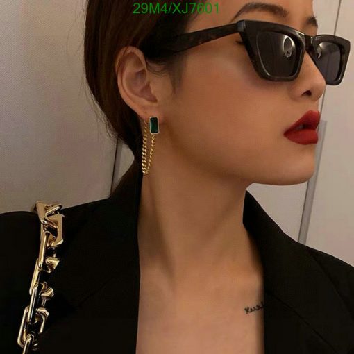 Woman with sunglasses, red lipstick, and green earrings.