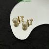 Gold pearl earrings on reflective surface.