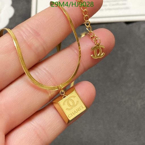 Gold designer logo necklace held in fingers.