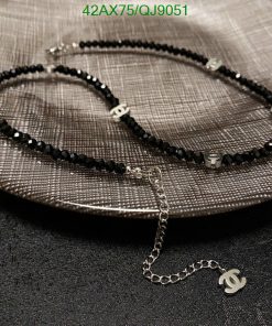 Black beaded necklace with logo charm on textured surface.