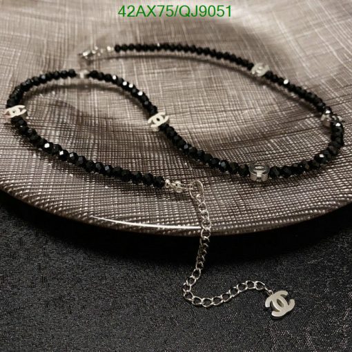 Black beaded necklace with logo charm on textured surface.