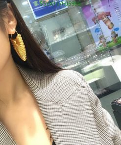 Woman wearing golden leaf earring and houndstooth blazer.