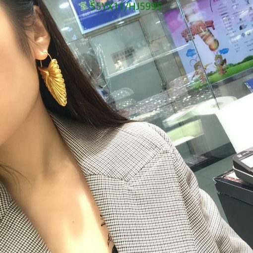 Woman wearing golden leaf earring and houndstooth blazer.