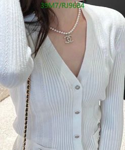 Woman wearing white cardigan and pearl necklace.