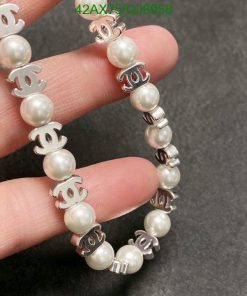 Pearl bracelet with silver logo charms on grey background.