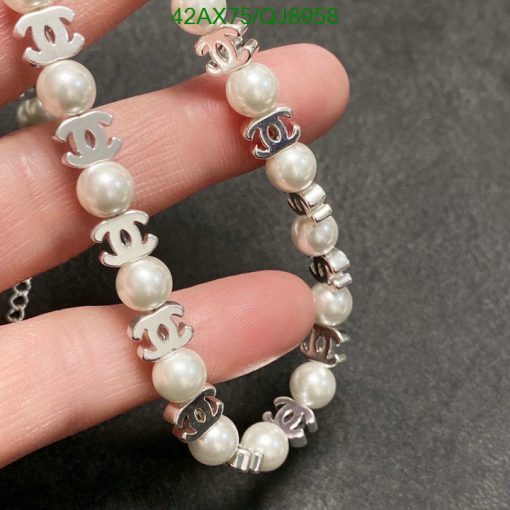 Pearl bracelet with silver logo charms on grey background.