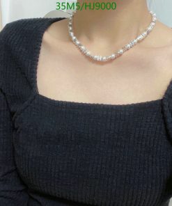 Woman wearing black sweater and pearl necklace.