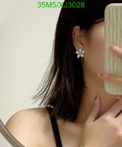 Woman showcasing pearl flower earring in mirror selfie.