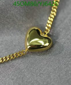 Gold heart pendant on chain against gray fabric.