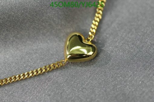 Gold heart pendant on chain against gray fabric.