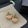 Gold earrings with pink stones on gray fabric.