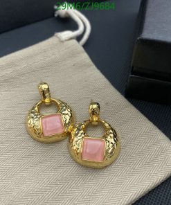 Gold earrings with pink stones on gray fabric.