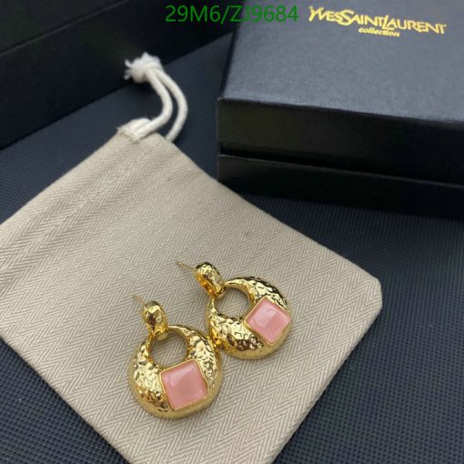 Gold hoop earrings with pink stone on fabric surface.