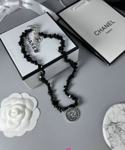 Chanel black bead necklace with logo on marble surface.