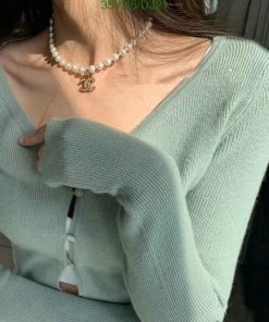 Woman wearing pearl necklace and green sweater.