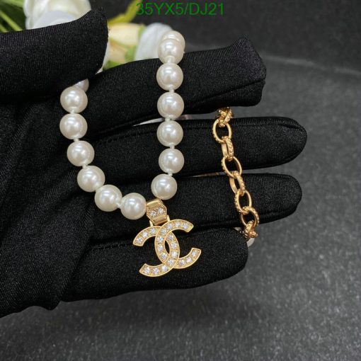 Elegant pearl bracelet and gold pendant on black glove.