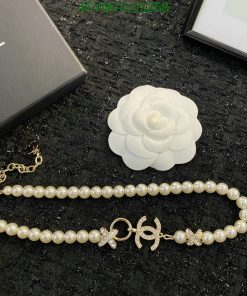 Pearl bracelet and white flower brooch on textured surface.