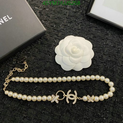 Pearl bracelet and white flower brooch on textured surface.