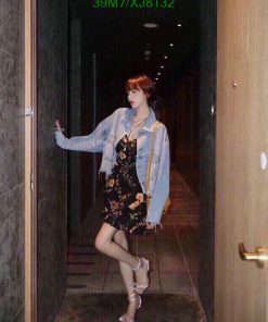 Woman posing in hallway wearing floral dress and denim jacket.