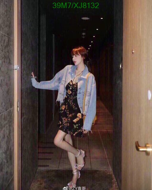 Woman posing in hallway wearing floral dress and denim jacket.