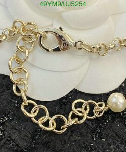 Gold chain bracelet with pearl charm on black texture.