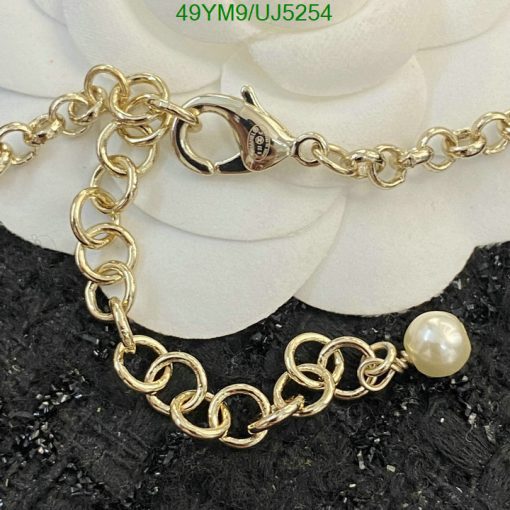 Gold chain bracelet with pearl charm on black texture.