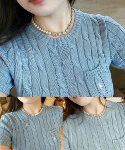 Woman wearing blue cable knit sweater with pearl necklace.