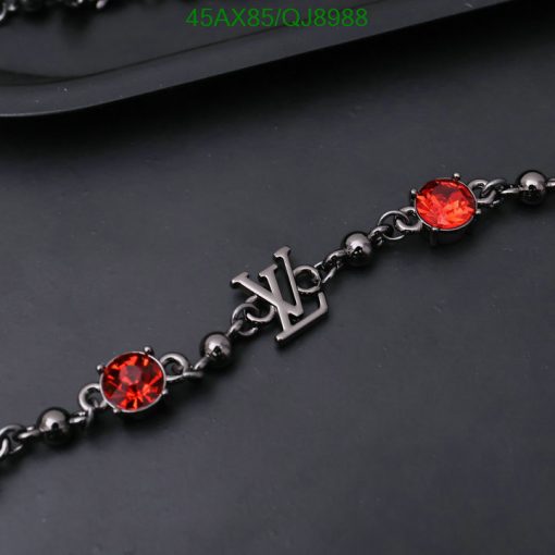 Red gemstone bracelet with initial charm on dark background.