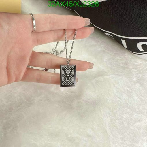 Hand holding V letter pendant over fuzzy background.